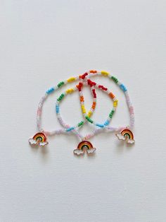 three bracelets with rainbow beads and silver bells on white background, close up photo