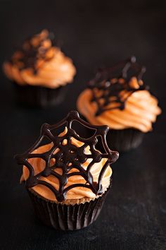 three cupcakes with chocolate frosting and spooky spider web decorations on them