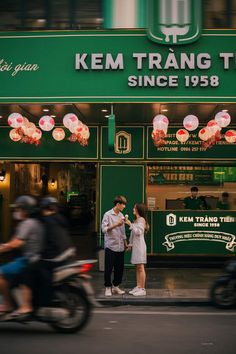 a man and woman standing in front of a store on the street with motorcycles passing by