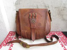 Beautiful unique vintage handbag from '60s. The bag is made of natural light brown leather and brass. The bag is beautifully decorated with brass, stamped ornaments and fringes. One main compartment and one big pocket inside the handbag. Dimensions: Width: 10.8 inches (27.5 cm); Height: 9 inches (23 cm); Depth: 2.4 inches (6 cm). It weighs: 620 grams. The bag has only one adjustable strap. It can be worn on the shoulder or across the body. This item is in good vintage condition, used. The bag is Stamped Ornaments, Leather Strap Bag, Cross Body Handbag, Leather And Brass, Tooled Leather Purse, Vintage Handbag, Light Brown Leather, Big Pocket, Strap Bag