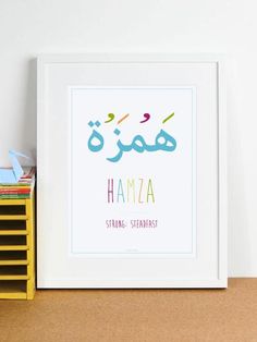 a white framed print with the words hamza in different colors on it next to a stack of books