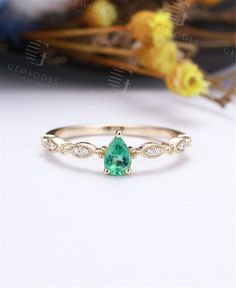 an emerald and diamond ring sitting on top of a white table next to dried flowers