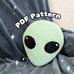 a green alien stuffed animal laying on top of a bed with the words pattern over it