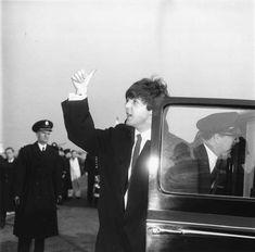 a black and white photo of a man in a suit waving to people from a car