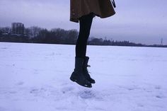 a woman jumping in the air on top of snow covered ground with her feet up