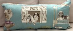 a blue pillow with dogs on it sitting on a couch in front of a window