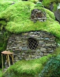 a small house made out of rocks and grass with a window in the center surrounded by trees