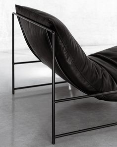 a black leather chaise lounge chair with metal frame and footrests on concrete flooring