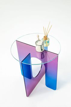 a purple and blue glass table sitting on top of a white floor next to a vase