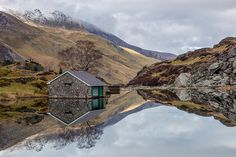 a small house sitting on top of a lake surrounded by mountains