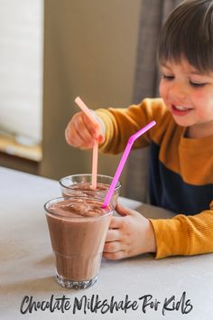 a little boy sitting at a table with a glass of chocolate milkshake