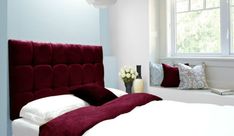 a bedroom with a red headboard and white bedding in front of a window