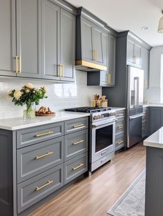 a kitchen with gray cabinets and gold pulls on the handles, white marble countertops and wood flooring