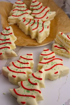 several pieces of christmas tree shaped cookies on a wooden platter next to two slices of cake