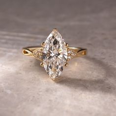 a yellow gold ring with a pear shaped diamond in the center and side stones on each band