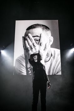 a man holding his hands to his face while standing in front of a large screen