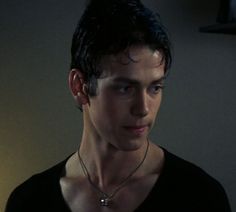 a young man wearing a necklace with a cross pendant on it's neck in a dimly lit room