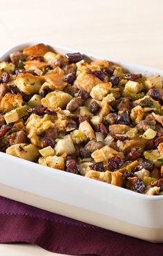 a casserole dish filled with stuffing and vegetables on top of a purple cloth