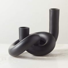 two black vases sitting next to each other on a white counter top, one has an oval shape and the other is curved