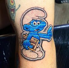 a cartoon character tattoo on the leg of a person's leg, with an image of smurf holding a book