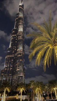 the burj tower is lit up at night with palm trees in foreground