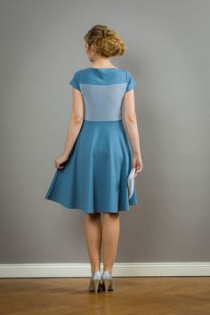 a woman in a blue dress is standing against a wall and looking at the floor