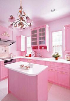 a kitchen with pink cabinets and white counter tops, chandelier above the island