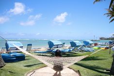 a hammock on the beach with lounge chairs and people in the water behind it