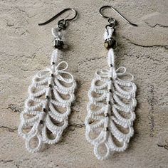 white crocheted leaf earrings with black beads on them sitting on a stone surface