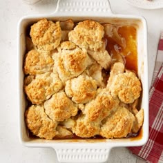 a casserole dish filled with biscuits next to a red and white checkered napkin