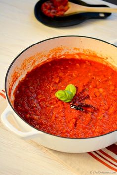 a white pot filled with red sauce on top of a wooden table