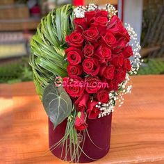 a vase filled with red roses on top of a wooden table covered in greenery