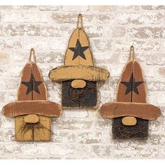 three wooden scarecrows hanging on a brick wall, one wearing a hat and the other holding a star