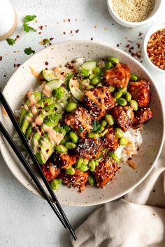 a white plate topped with meat and veggies covered in sauce next to two chopsticks