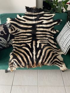 a zebra skin rug sitting on top of a green couch next to pillows and plants