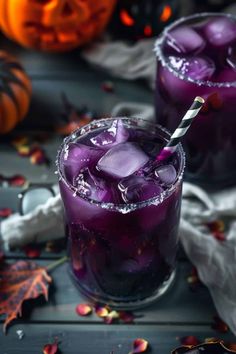 two glasses filled with purple liquid and ice on top of a table next to pumpkins