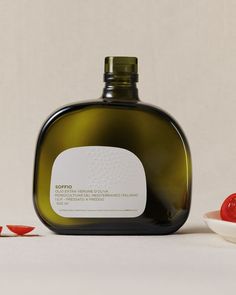 a bottle of olive oil next to two small pieces of red pepper on a white surface