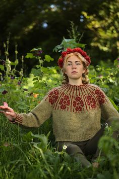 a woman is sitting in the grass with her hands out and wearing a red flower crown