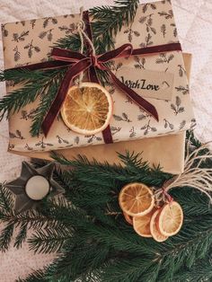 two wrapped presents with orange slices on them sitting next to christmas tree branches and candles