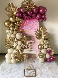 a happy birthday balloon arch with balloons and gold leaves on the top, in front of a pink backdrop