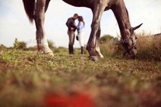 two people standing next to a horse eating grass