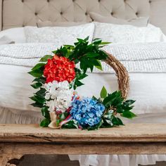 a wreath with flowers on top of a wooden table in front of a white bed