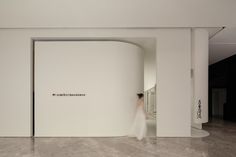 a woman walking through a white room with a large wall and logo on the side