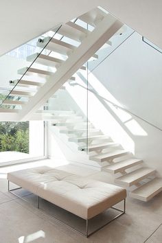 a white couch sitting under a stair case next to a glass wall and window on top of the stairs