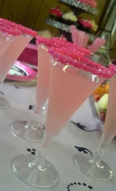 three martini glasses filled with pink liquid on top of a white tablecloth covered table