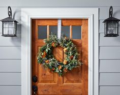 a wooden door with a wreath hanging on it's side next to two lanterns