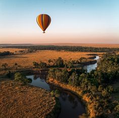 a hot air balloon flying over a river in the middle of a lush green field