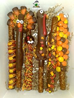 an assortment of candy sticks with faces on them in a cardboard box filled with oranges, yellow and brown candies