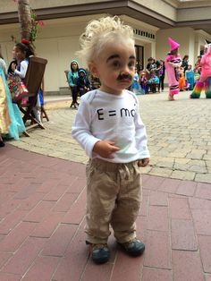 a little boy with a moustache on his face standing in front of a crowd