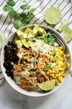 a bowl filled with taco salad and garnished with cilantro, corn, black beans, avocado, lime wedges